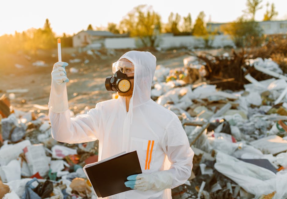 A close-up of a metal bin filled with tightly packed, partially burned cardboard boxes and packaging materials, with orange flames and wisps of smoke rising from the debris. The cardboard shows variou